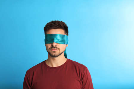 128859805 young man with blindfold on blue background space for